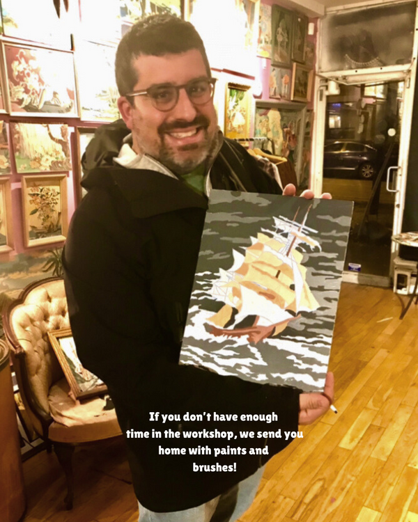 Man holding a painting of a sailboat in a workshop setting
